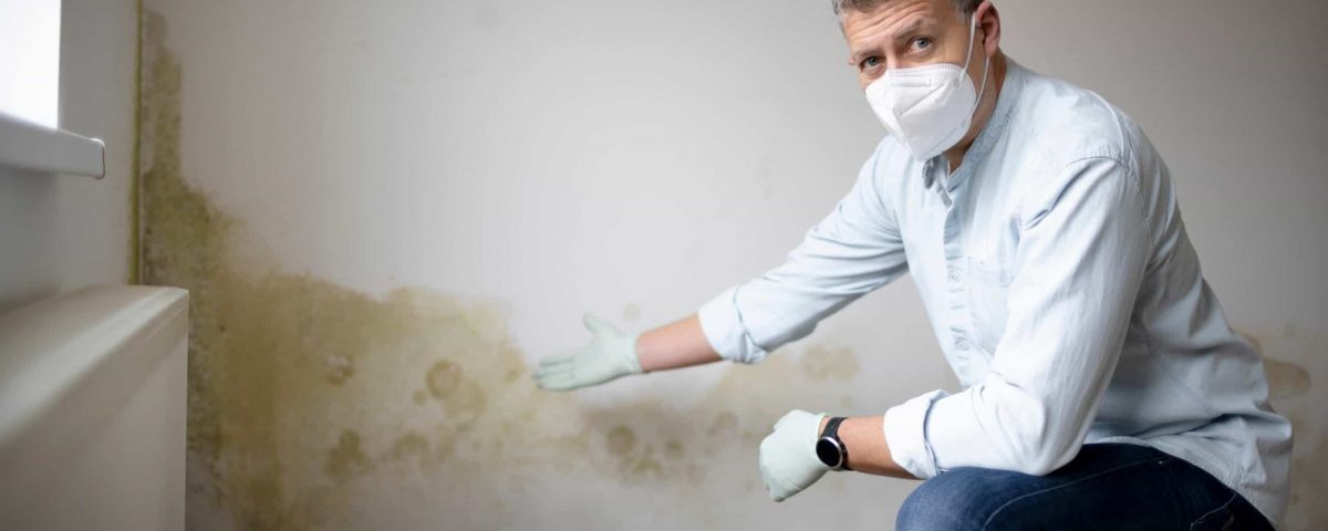 Fachmann mit Atemschutz begutachtet Feuchtigkeitsflecken an Wand – Professionelle Feuchtigkeitsdiagnose